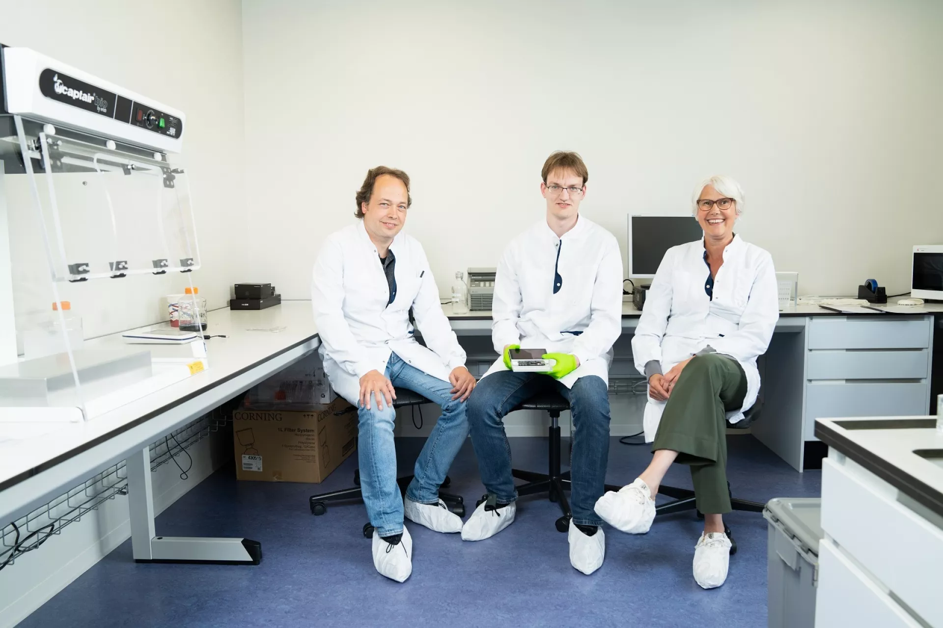 Twee mannen en vrouw van Certe in labjas zittend in laboratorium