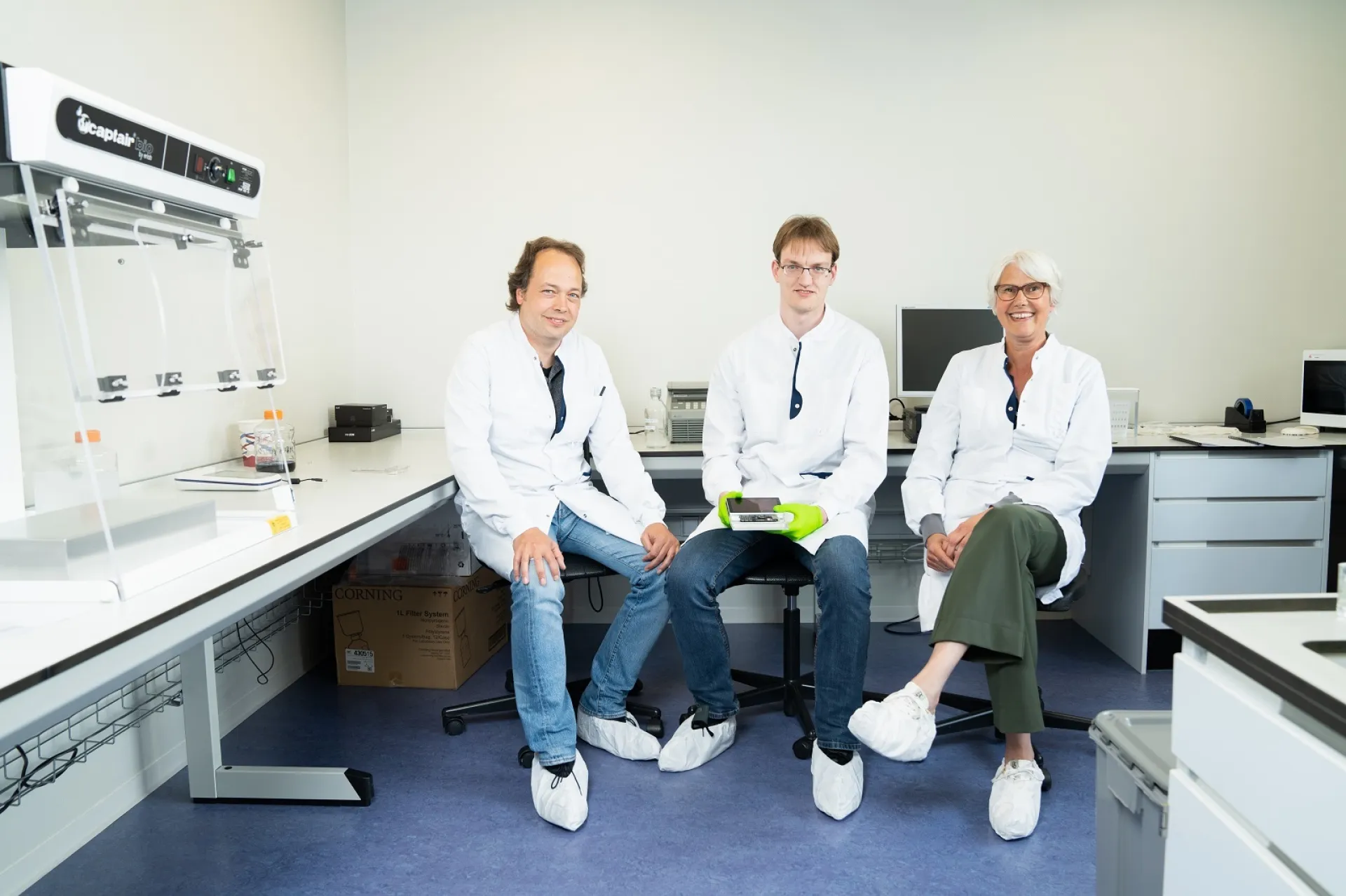 Twee mannen en vrouw van Certe in labjas zittend in laboratorium