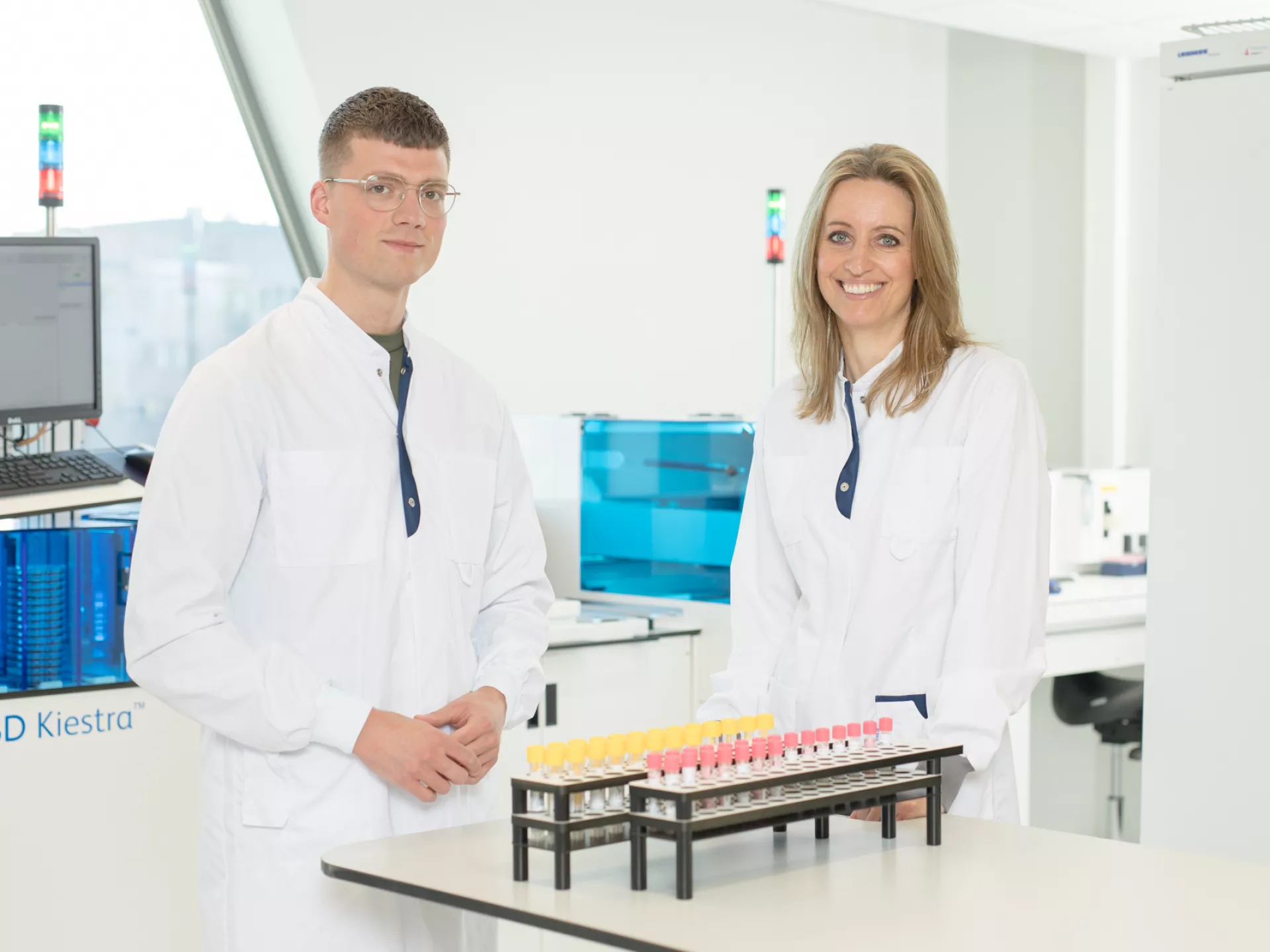 Man en vrouw analisten medische microbiologie in labjas bij rekje buizen