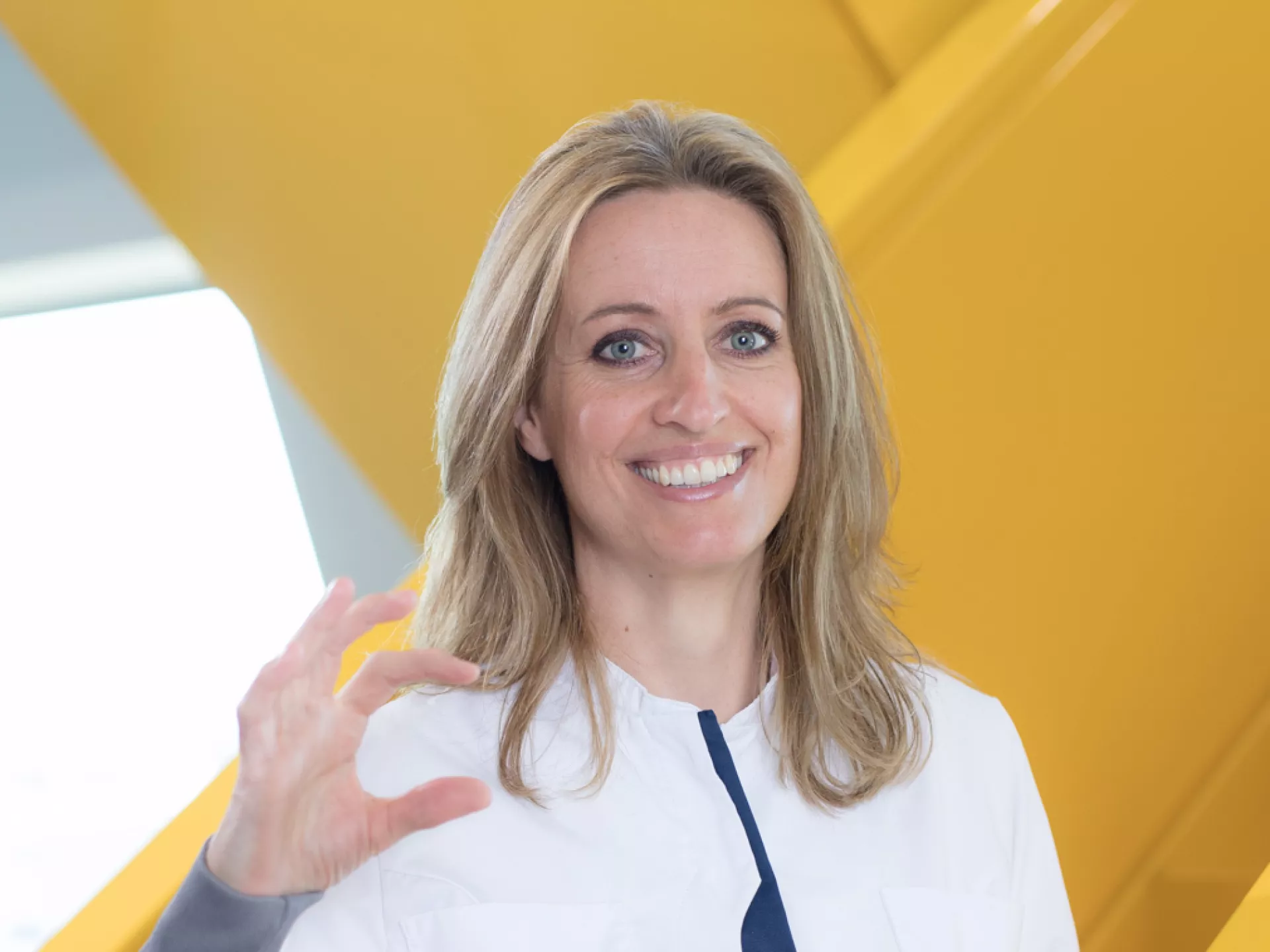 Dame op gele trap in labjas met ZekerCerte gebaar