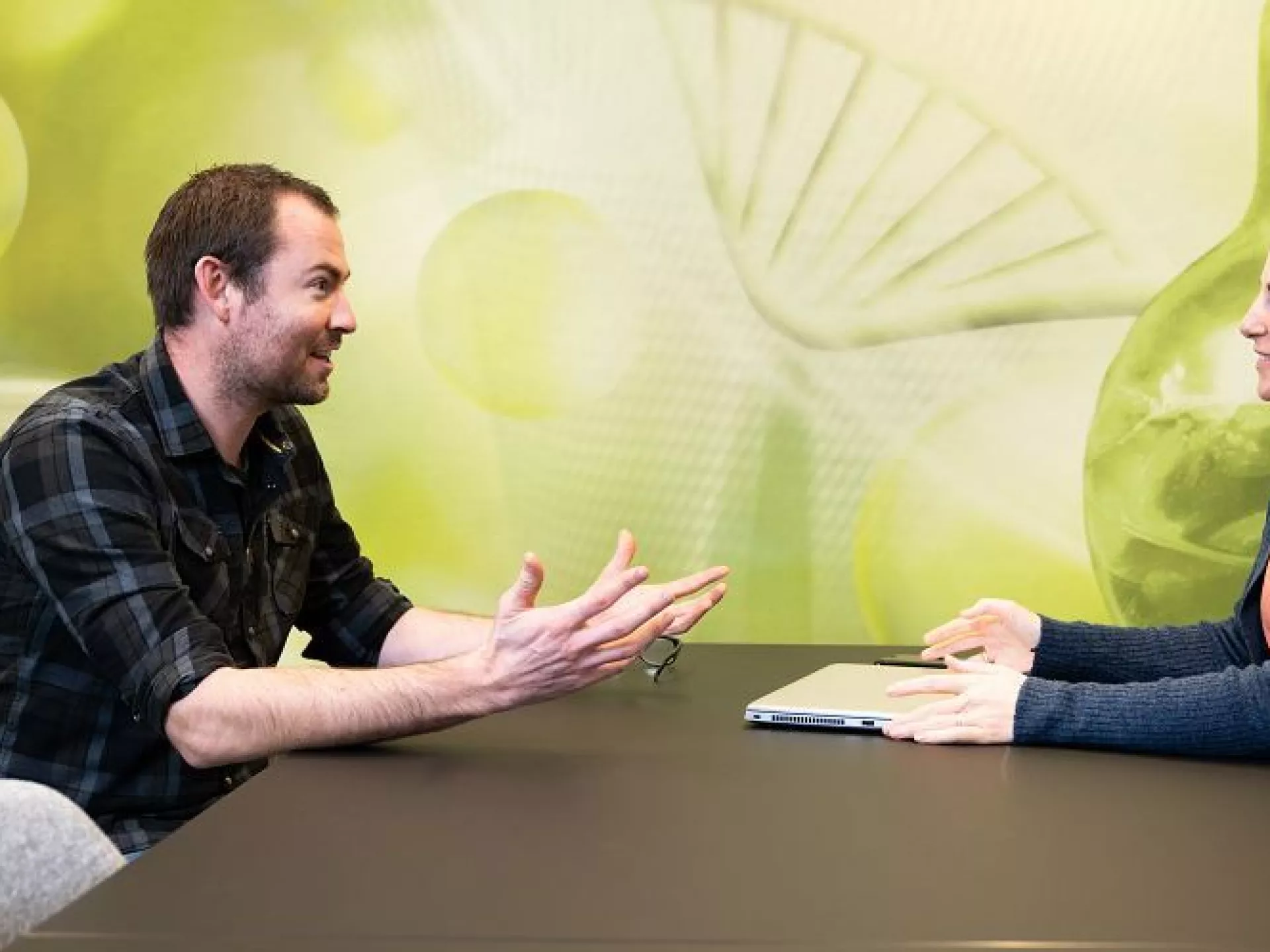 Man en vrouw pratend aan tafel voor groene wand