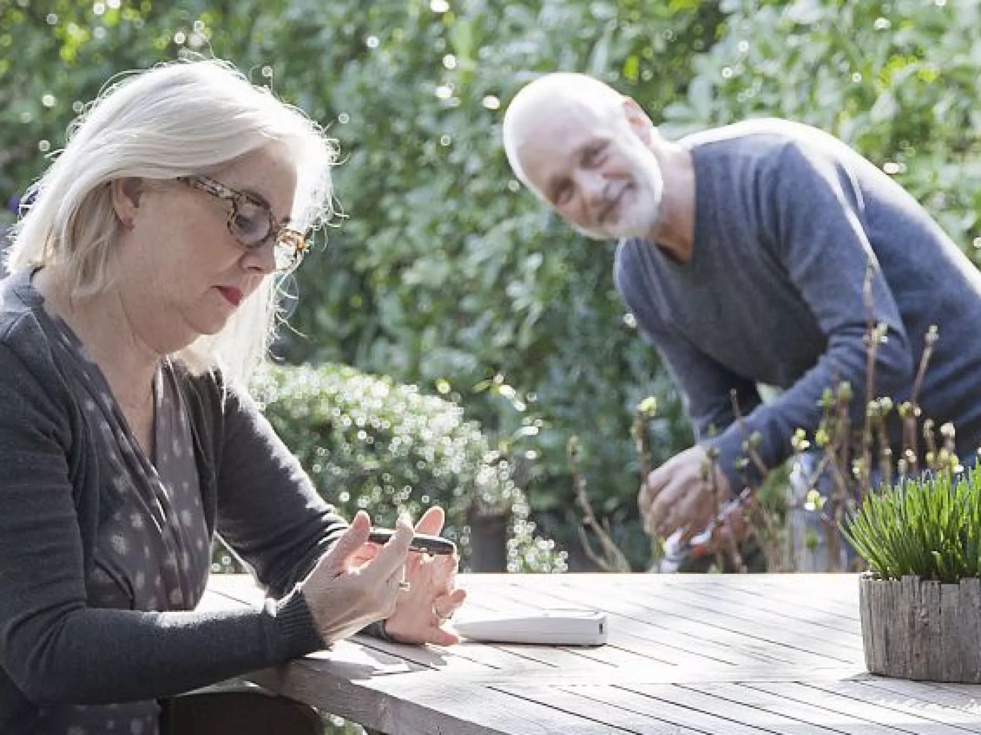 Dame in tuin aan tafel aan het zelfmeten, man op achtergrond