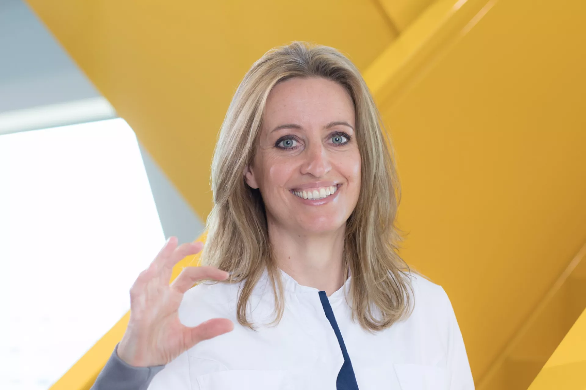 Dame op gele trap in labjas met ZekerCerte gebaar