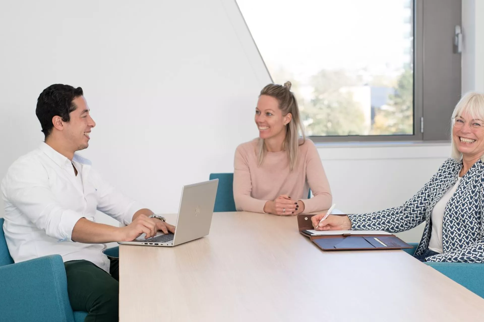 Overleg drie mensen aan een tafel in blauwe stoelen met laptop