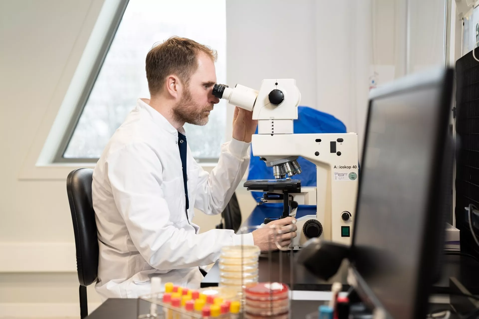Joppe van Duin achter microscoop naast computerscherm