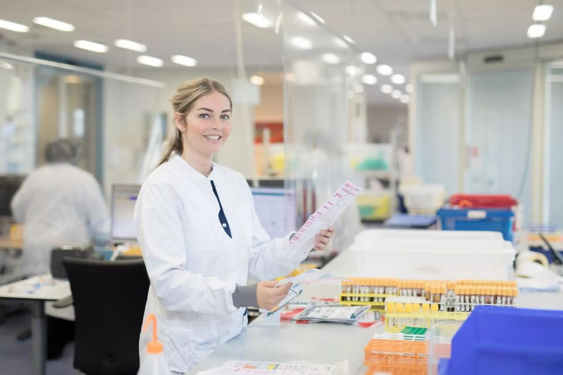 Dame in labjas op laboratorium bij rekjes met buizen met papier in de hand