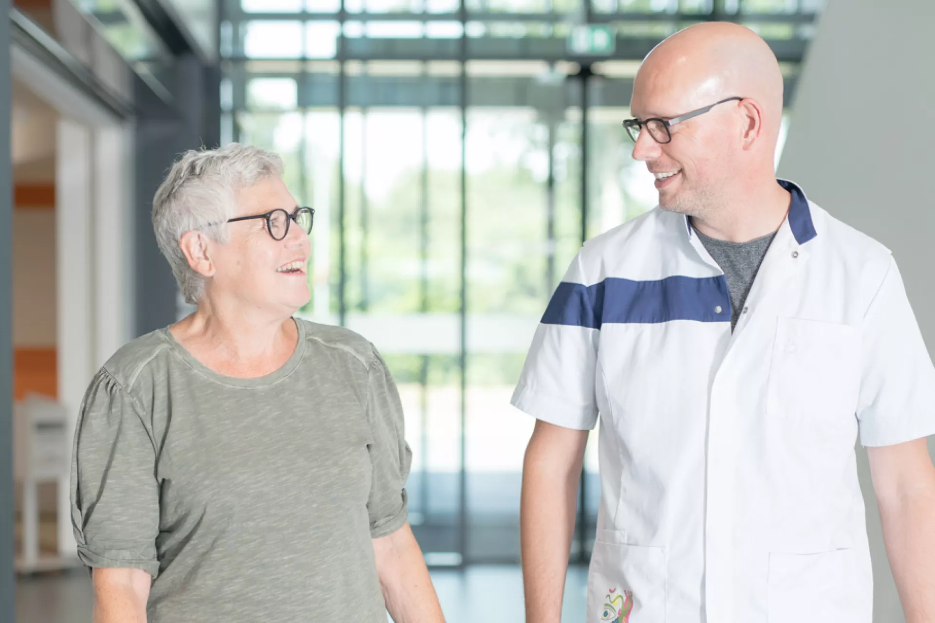 Patiënt en medewerker Certe lopend in gang elkaar aankijkend