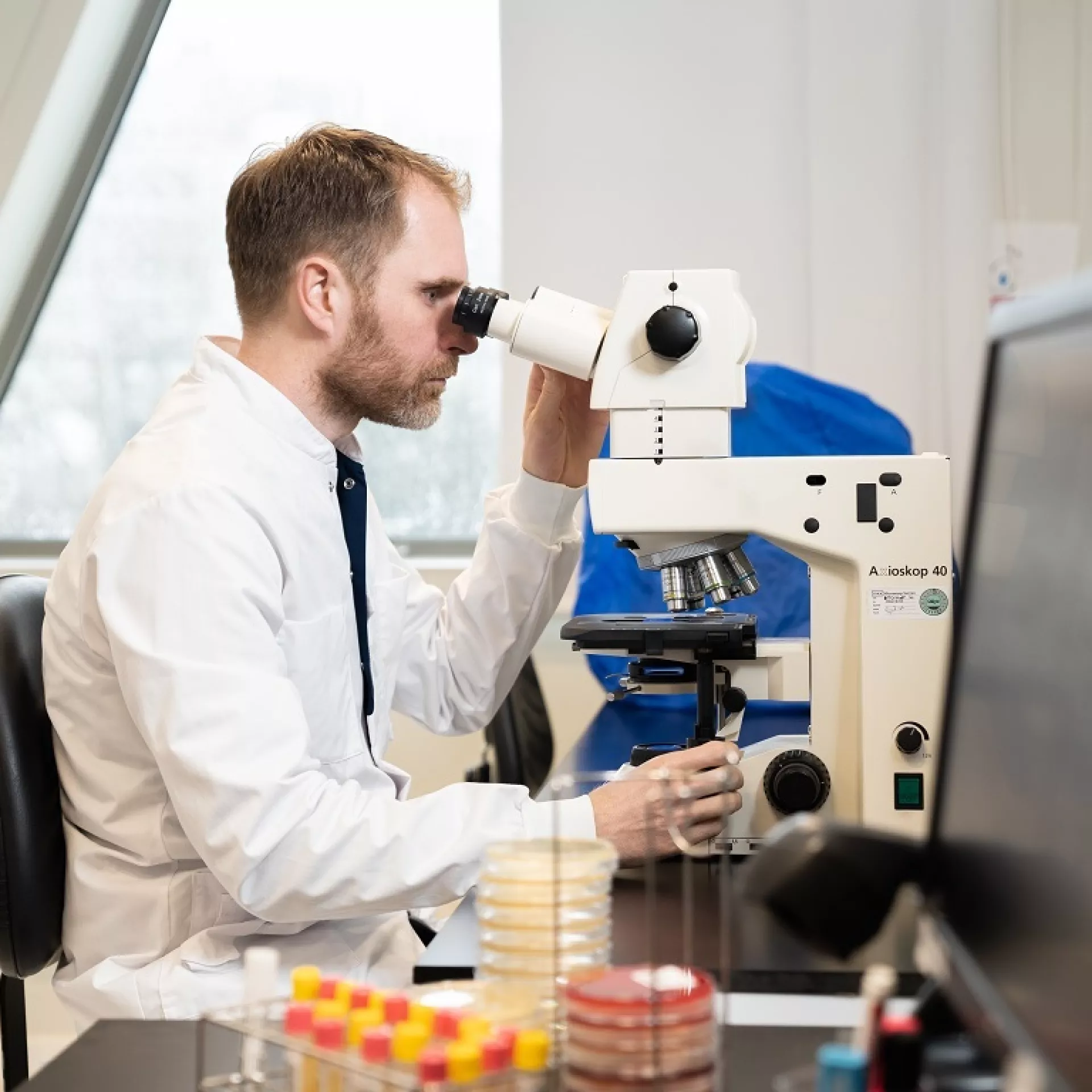 Joppe van Duin achter microscoop naast computerscherm