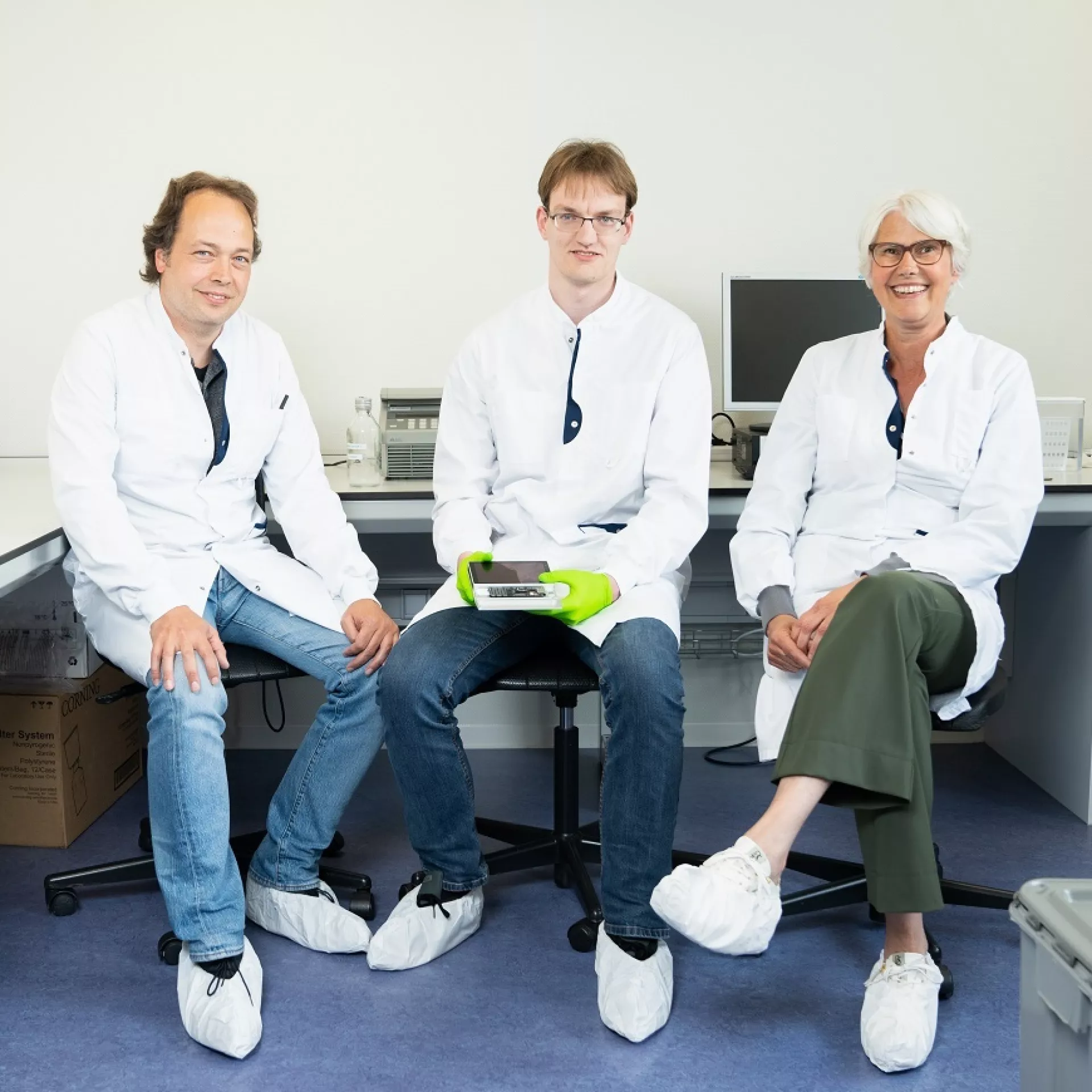 Twee mannen en vrouw van Certe in labjas zittend in laboratorium